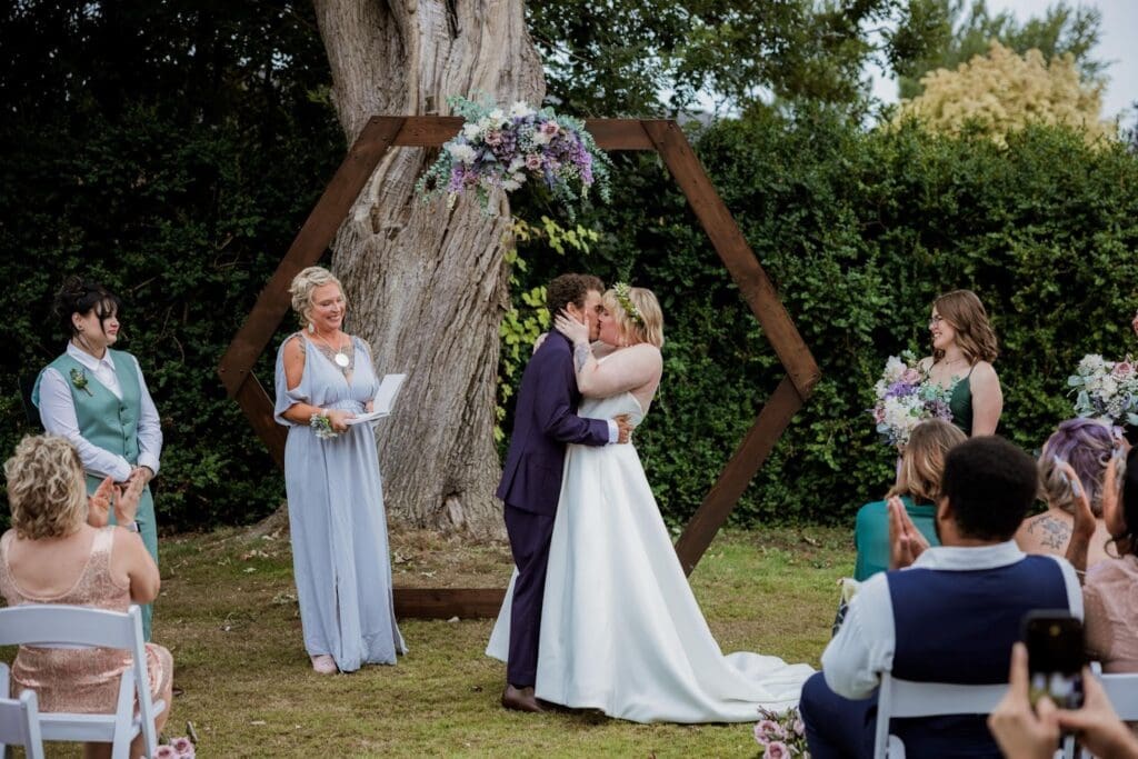 First kiss at the hexagon arch arch in an outdoor barn wedding venue