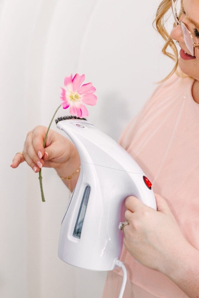 woman using clothes steamer on pink silk cosmos flower